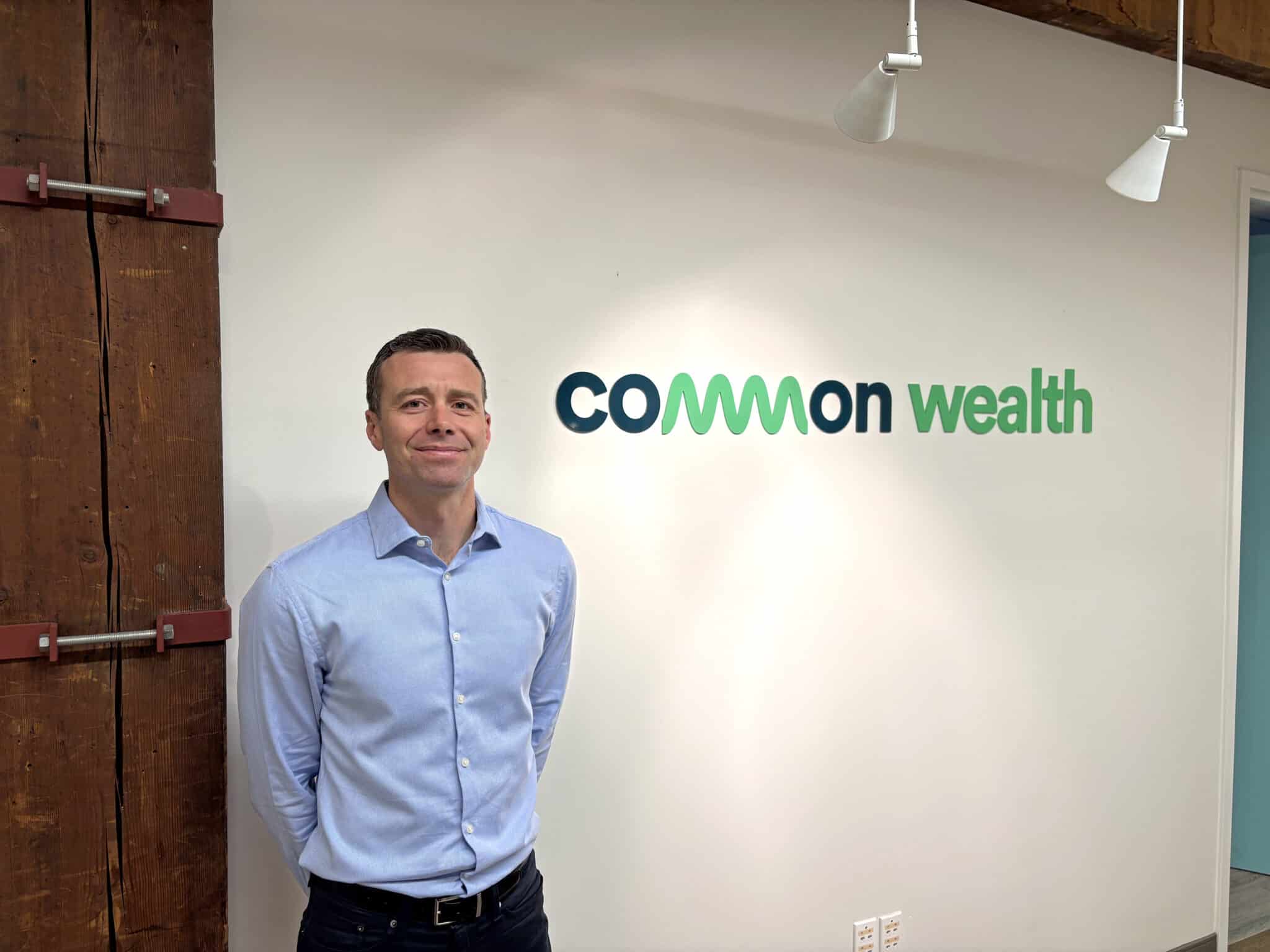 Alex Mazer, co-founder and CEO of Common Wealth, standing in front of the Common Wealth logo at the company's Toronto office.