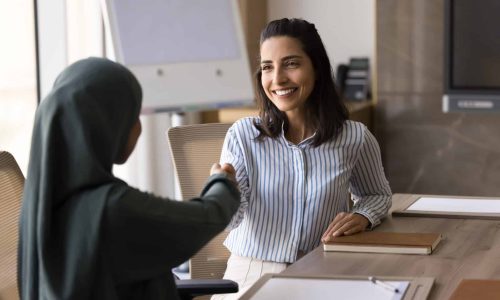 Two smiling multicultural businesswomen shake hands start meeting in office, express respect for teamwork, getting professional company service.