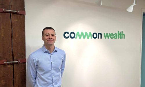 Alex Mazer, cofondateur et PDG de Common Wealth, debout devant le logo de Common Wealth dans le bureau de Toronto de l’entreprise.